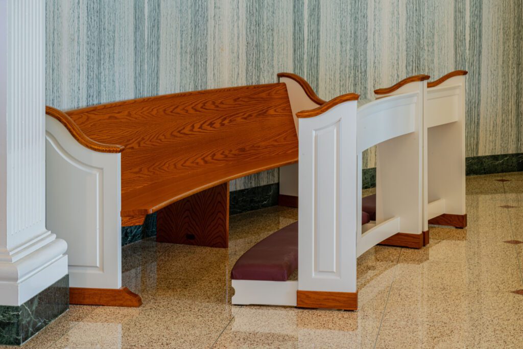 A curved church pew with a golden brown stain and white pew ends with a matching padded kneeling pad in front of it.