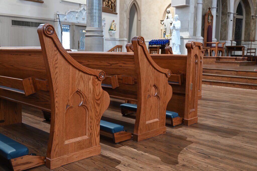 Wooden church pews with blue church kneelers in front of them.